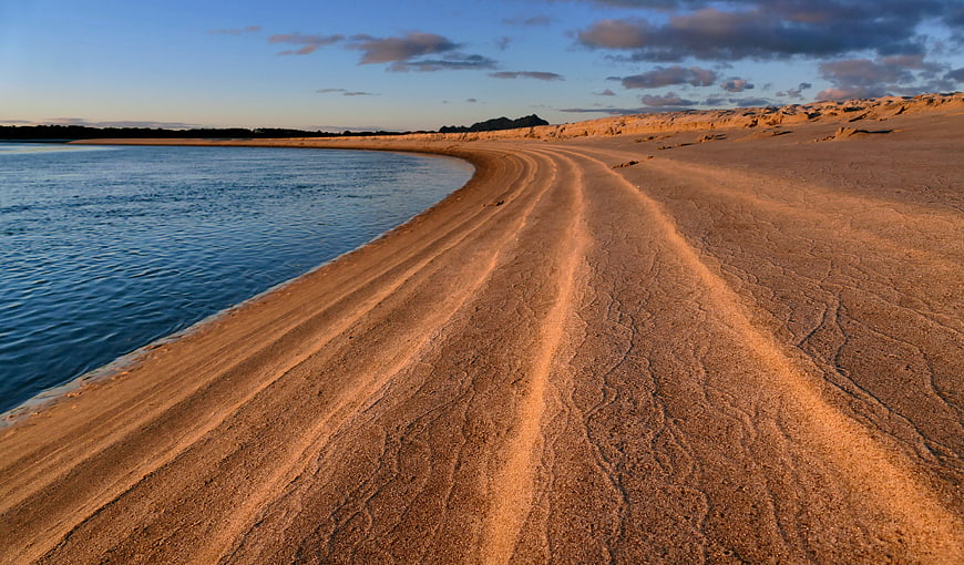 Golden sand dunes meeting calm blue water at sunset