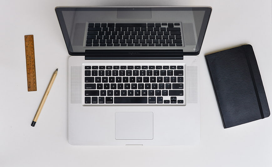 Top view of laptop, notebook, pencil, and ruler on white desk