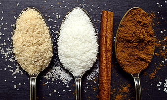 Spoons of brown sugar, white sugar, and cinnamon on dark slate