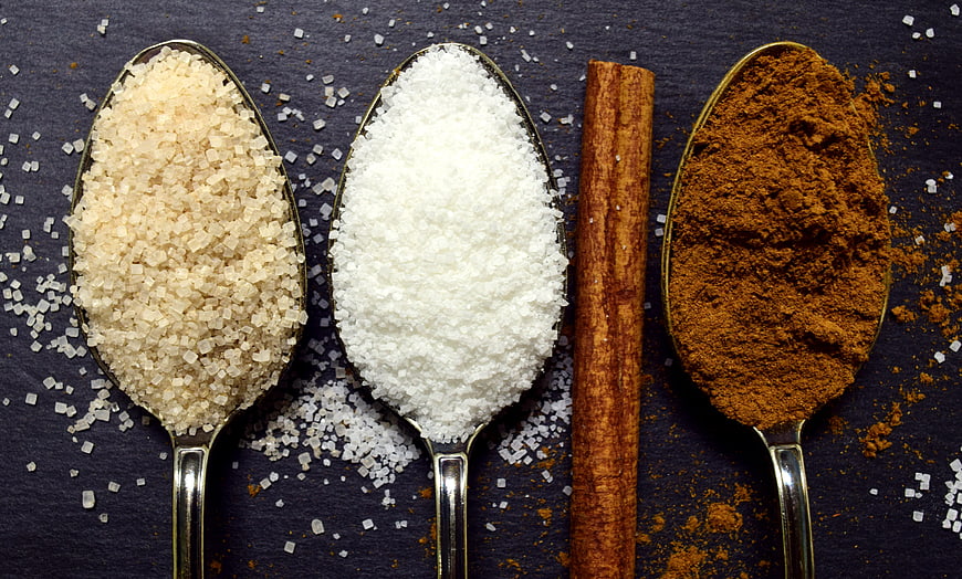 Spoons of brown sugar, white sugar, and cinnamon on dark slate