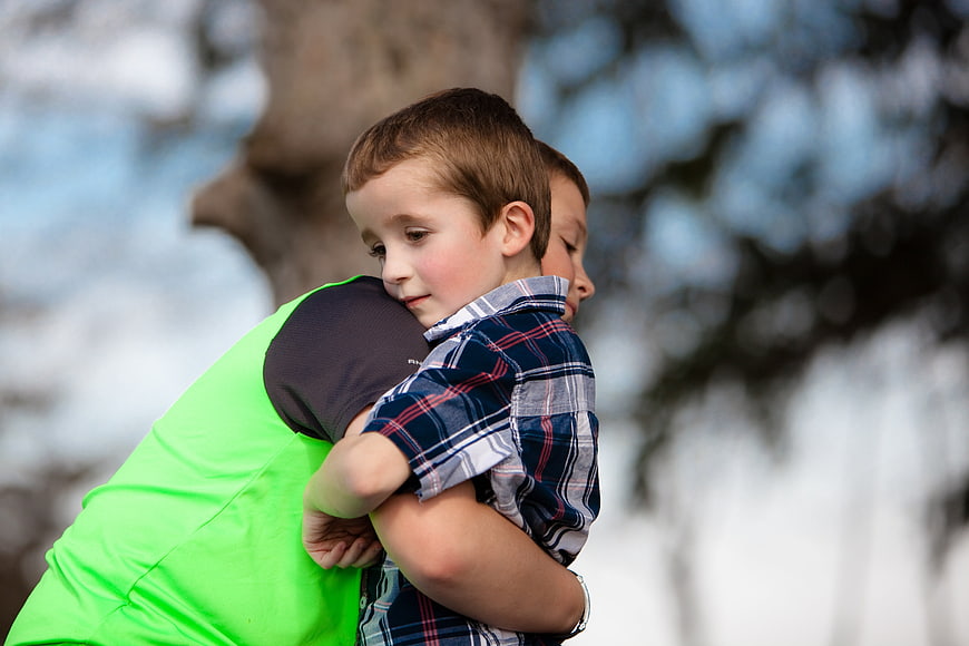 Two young boys hugging outdoors in a park