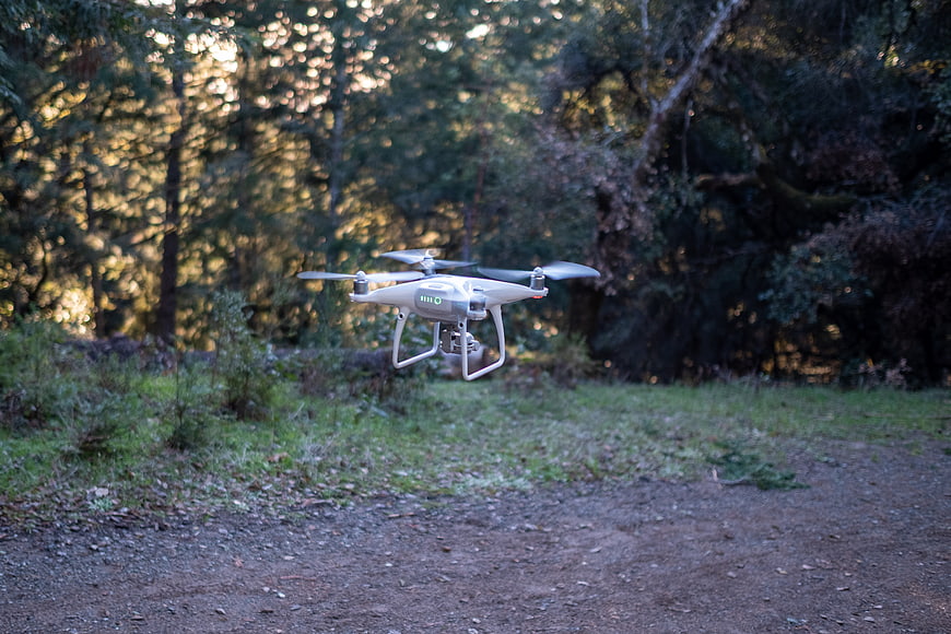 White drone hovering in forest clearing with sunlight