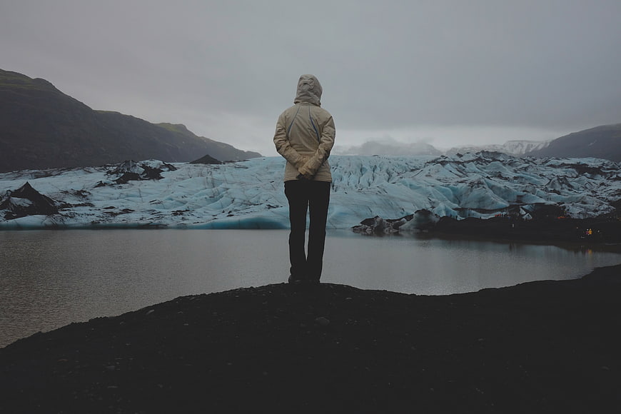 Person standing on black sand beach facing glacier lagoon