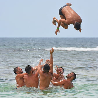 Group of men tossing friend into the air at the beach