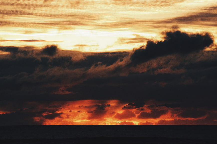Dramatic sunset over ocean with dark clouds and fiery orange sky