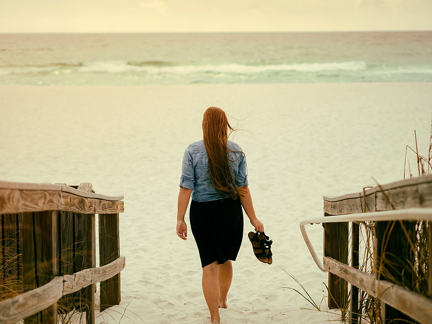 Woman Walking Down Wooden Stairs to White Sandy Beach
