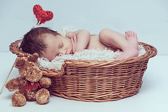 Sleeping newborn baby in wicker basket with teddy bear