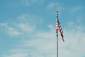 American flag waving against a blue sky with clouds