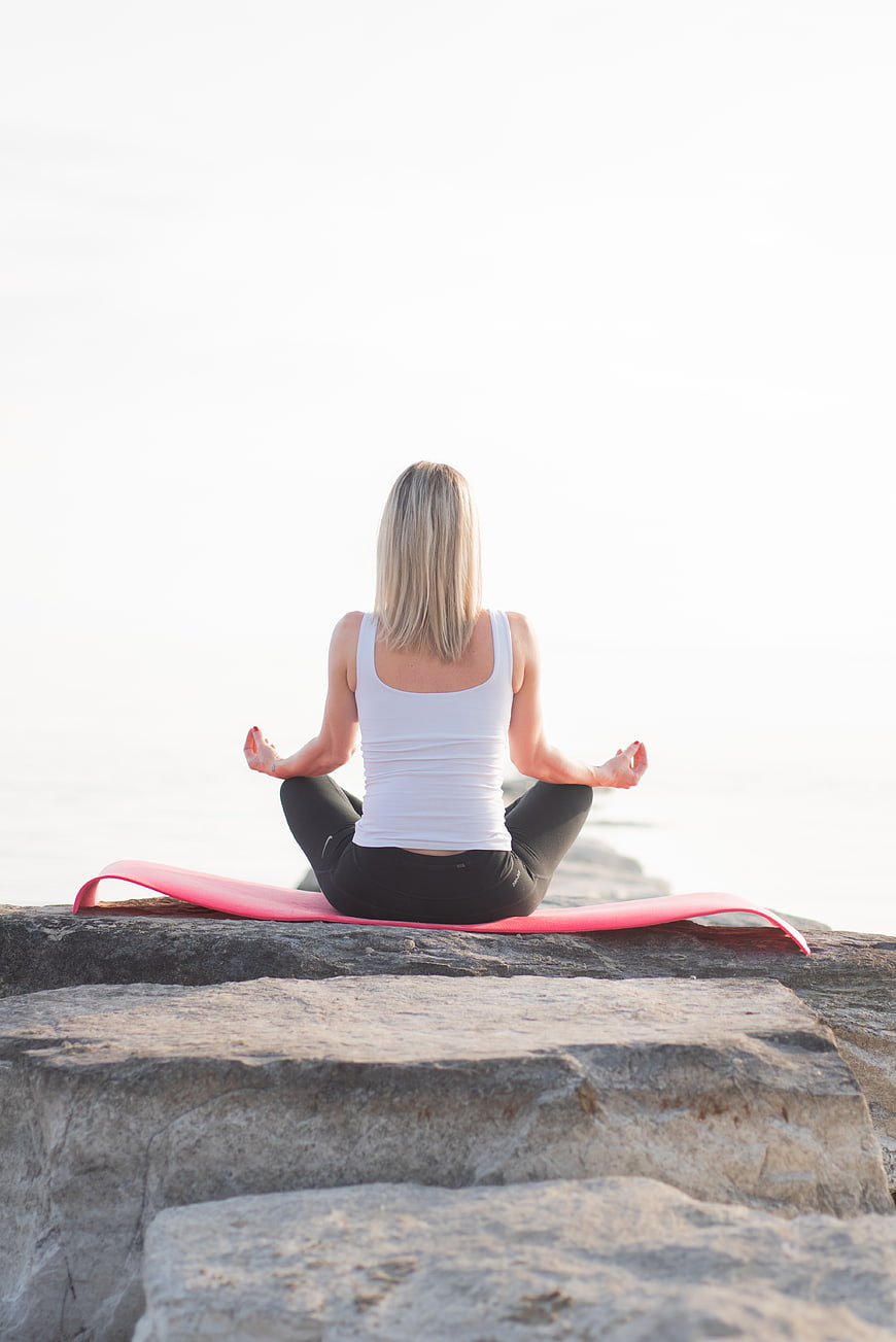 Woman meditating on yoga mat by the sea