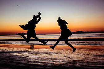 Silhouette of Two Women Jumping on Beach at Sunset
