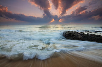 Dramatic sunset seascape with long exposure waves crashing on rocky shore