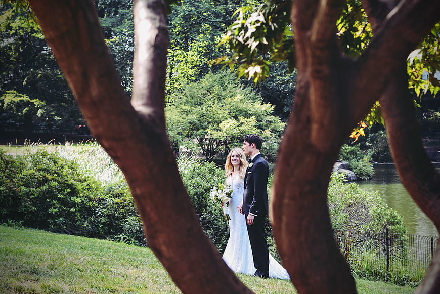 Wedding couple standing in park framed by tree branches
