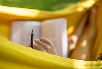 Woman studying in a yellow hammock with a book and pencil