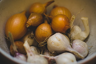 Fresh yellow onions and garlic bulbs in a rustic ceramic bowl