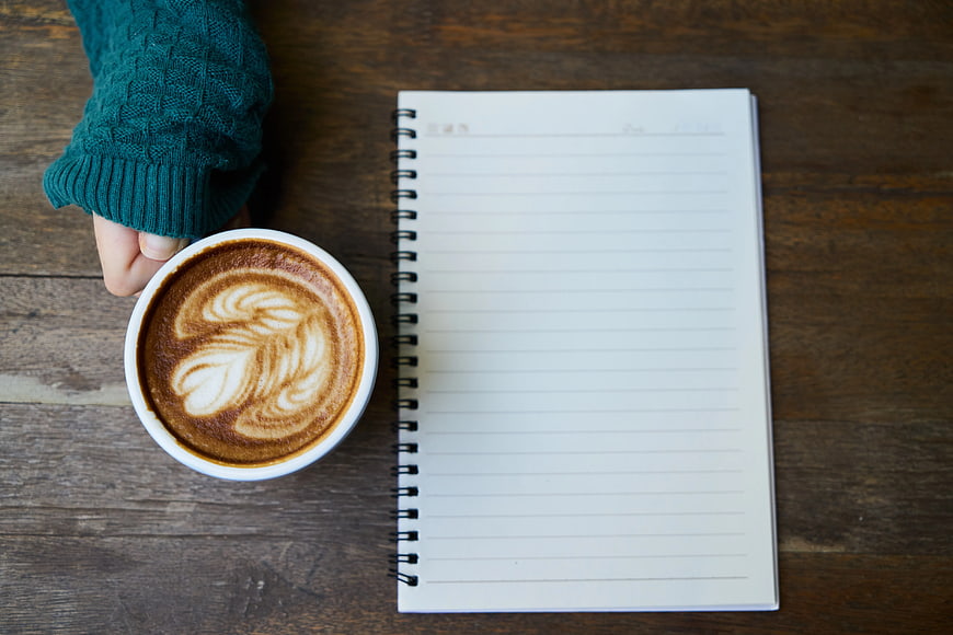 Flat lay of latte art coffee and blank notebook on wood