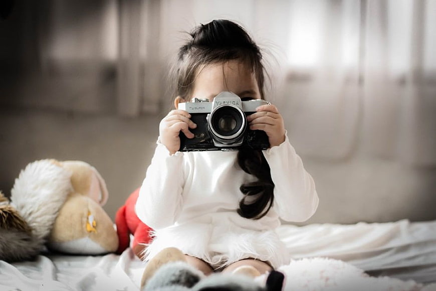 Toddler Girl Holding Vintage Camera on Bed