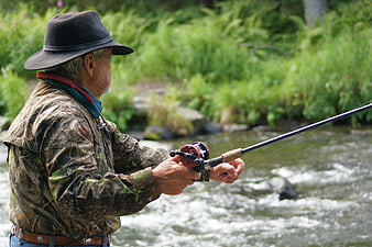 Senior man fly fishing in a rushing river wearing camouflage