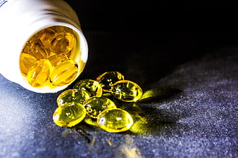 Spilled Golden Fish Oil Capsules From White Bottle On Dark Surface