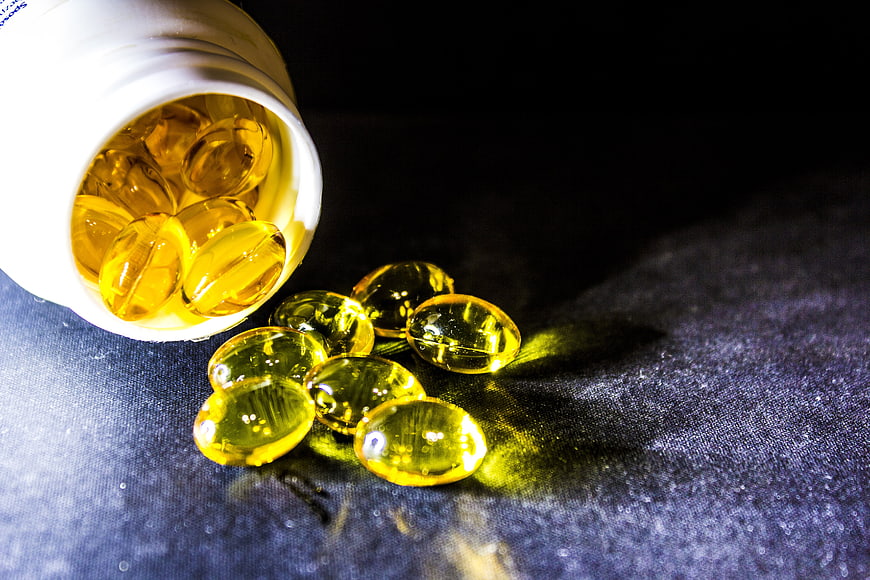 Spilled Golden Fish Oil Capsules From White Bottle On Dark Surface