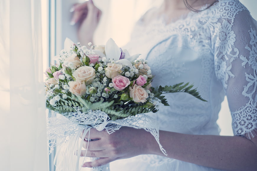 Bride holding pink and white rose bouquet in lace wedding dress