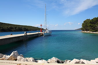 White sailboat docked at pier in turquoise Adriatic sea