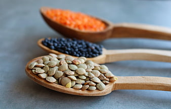 Three wooden spoons with green, black, and red lentils