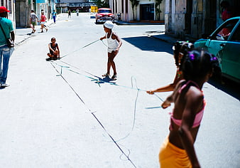 Children Playing Jump Rope on Sunny Street with Vintage Car