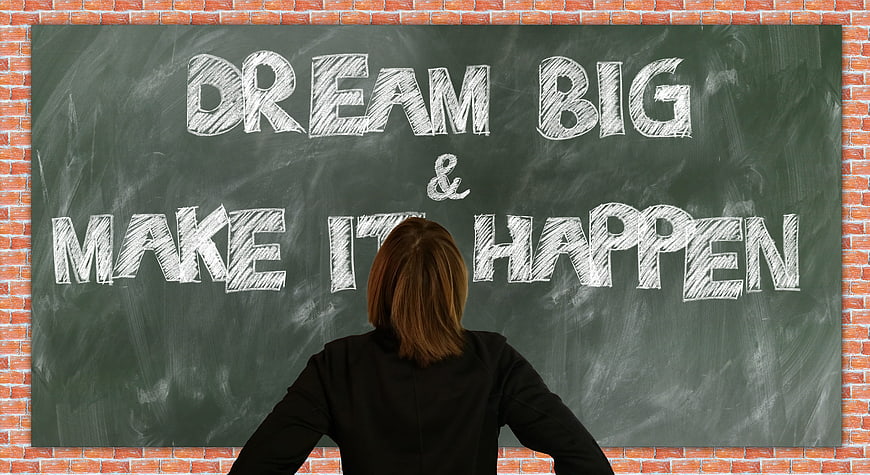 Woman standing before chalkboard with motivational quote dream big