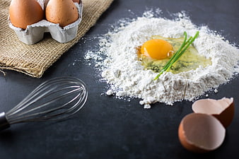 Baking ingredients with flour, eggs, and whisk on dark background