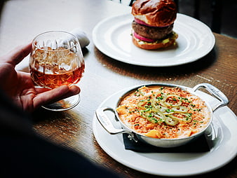 Hand holding whiskey glass with burger and mac and cheese on wooden table