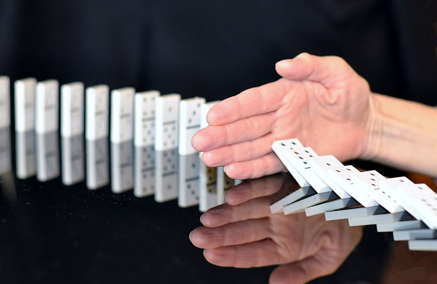 Hand stopping falling dominoes on black table