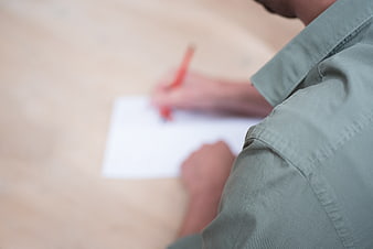 Close-up of person writing with red pen on white paper