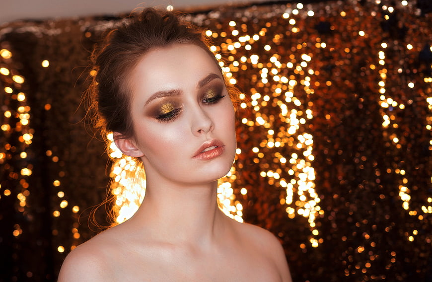 Elegant woman with gold makeup against glittering bokeh background