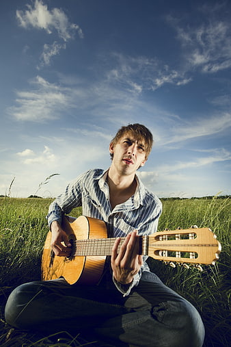 Young Man Playing Acoustic Guitar in Grassy Field