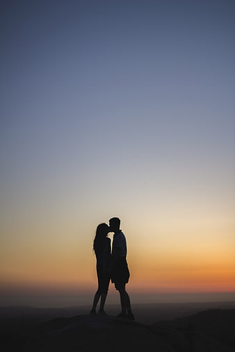 Silhouette of a couple kissing on a hilltop at sunset