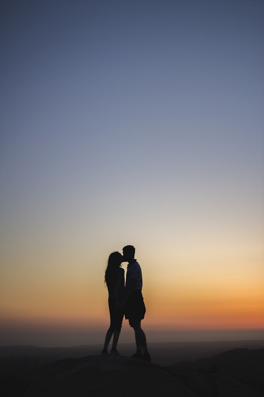Silhouette of a couple kissing on a hilltop at sunset
