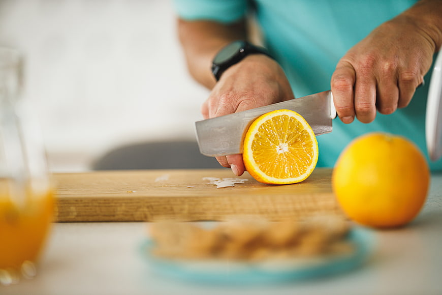 Man Cutting Fresh Orange on Wooden Board