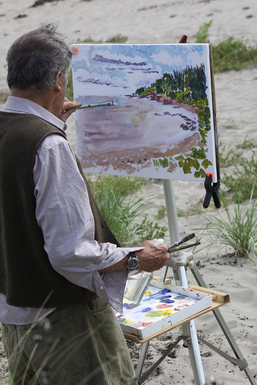 Senior artist painting landscape on easel at beach