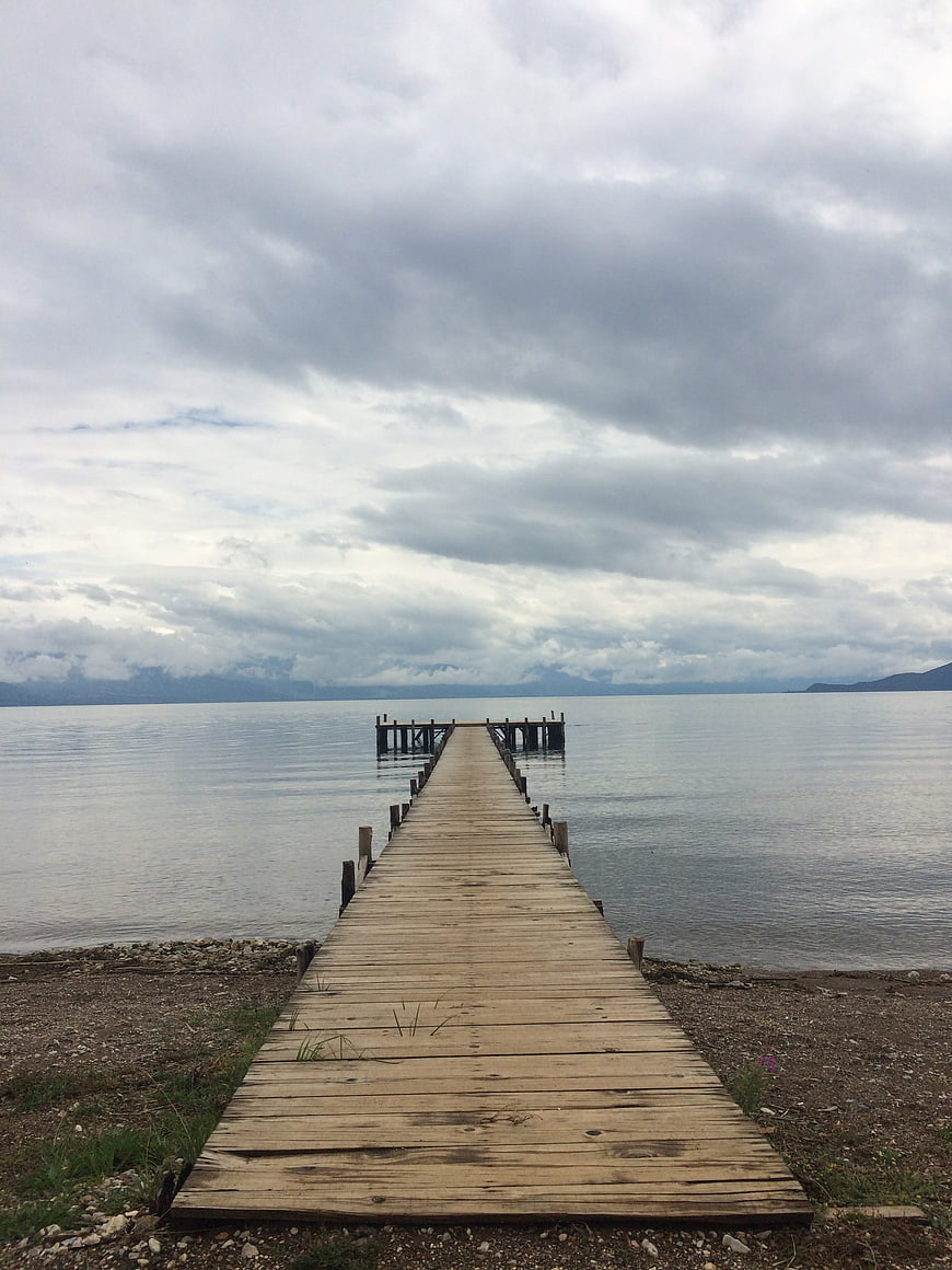 Wooden pier extending into calm lake under cloudy sky