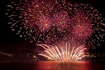 Vibrant Red and Gold Fireworks Display Over City River at Night