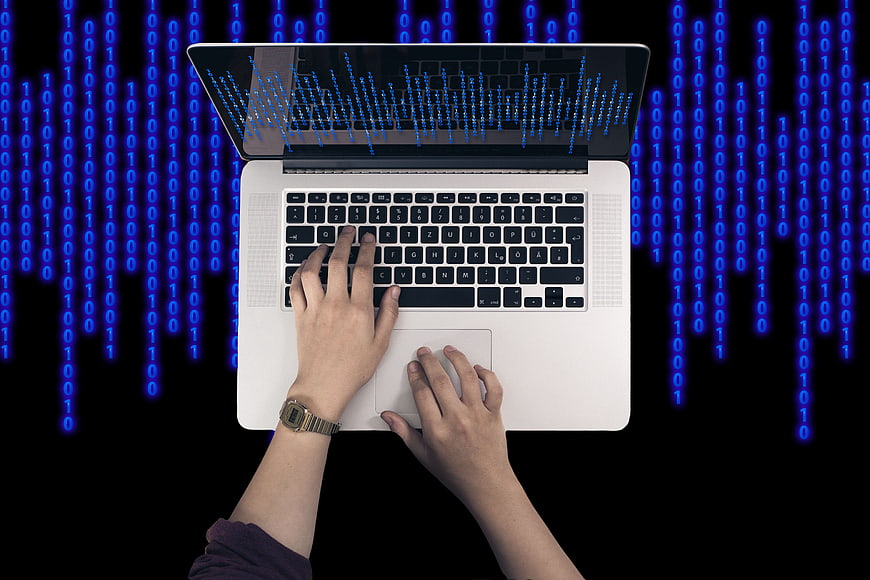 Hands typing on laptop with binary code background