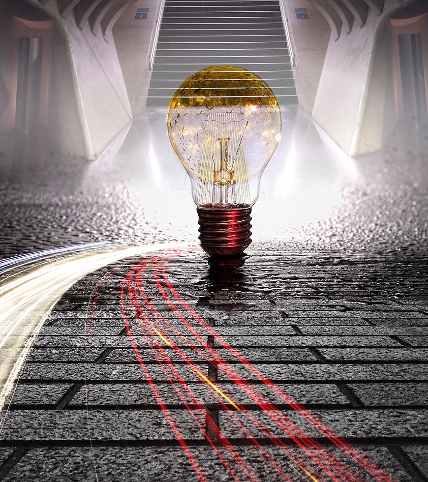Glowing light bulb on wet cobblestone street with light trails