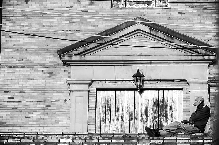 Black and white photo of man sleeping on urban building ledge