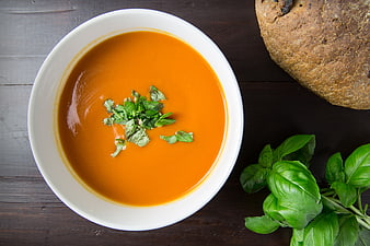 Overhead view of creamy tomato soup with fresh basil and rustic bread