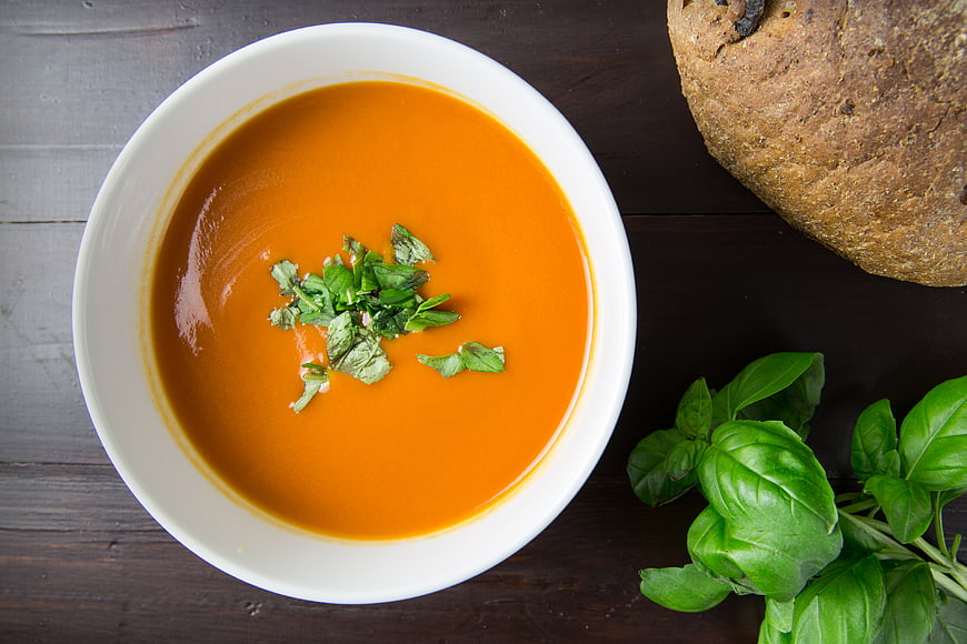 Overhead view of creamy tomato soup with fresh basil and rustic bread