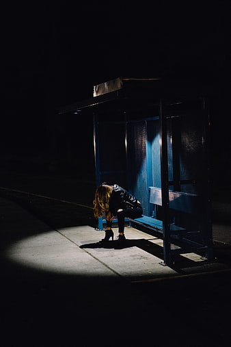 Woman sitting alone in spotlight at night bus stop