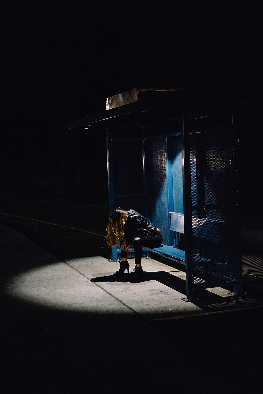 Woman sitting alone in spotlight at night bus stop