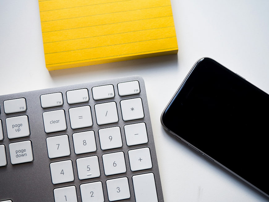 Minimalist workspace with keyboard, smartphone, and yellow notepad