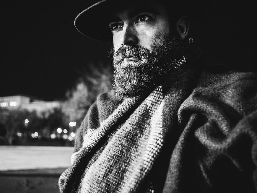 Black and white portrait of bearded man in hat at night