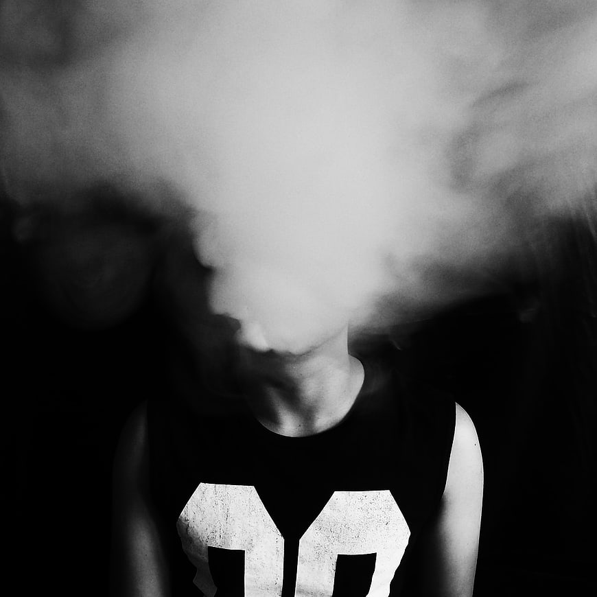 Man exhaling thick smoke in black and white portrait